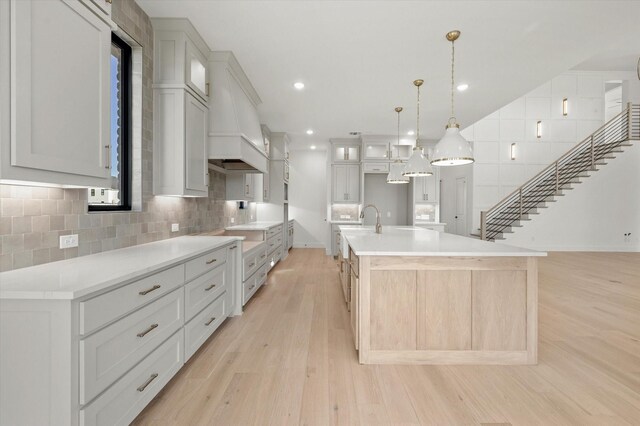 kitchen with decorative light fixtures, white cabinetry, decorative backsplash, light wood-type flooring, and a spacious island