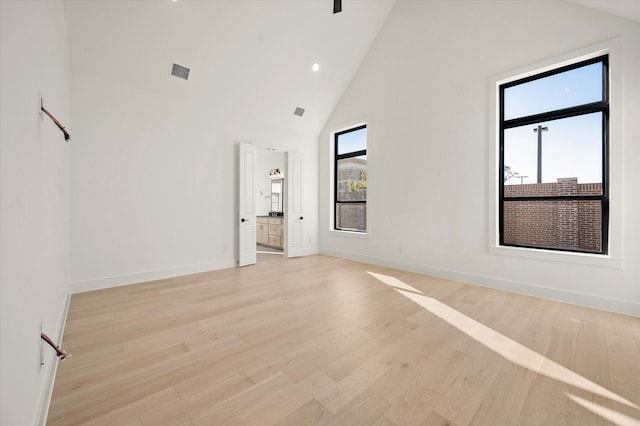 empty room with plenty of natural light, light wood-type flooring, and high vaulted ceiling