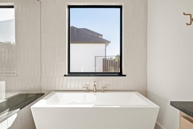 bathroom with plenty of natural light, a bathing tub, tile walls, and vanity