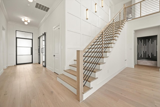 staircase featuring ornamental molding, a barn door, and wood-type flooring