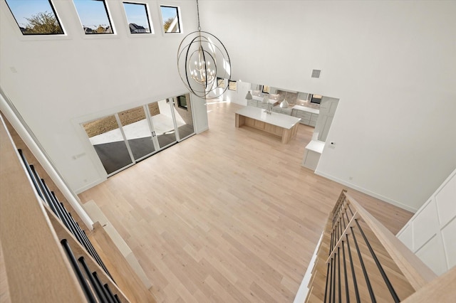 unfurnished living room featuring a healthy amount of sunlight, light wood-type flooring, an inviting chandelier, and a towering ceiling