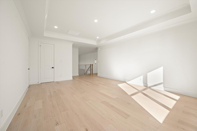 spare room with a tray ceiling and light wood-type flooring