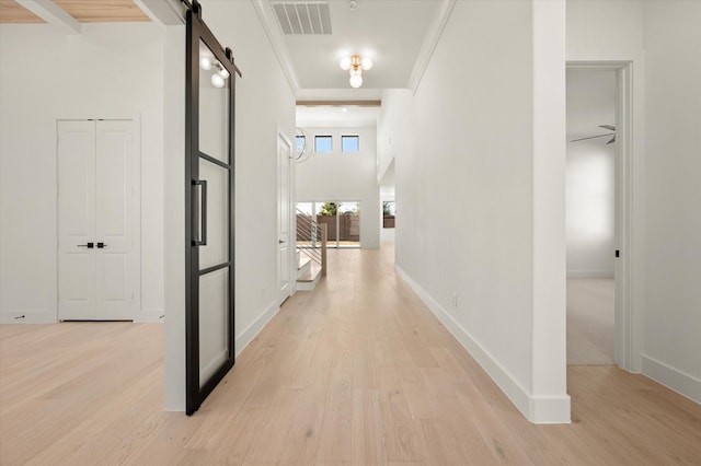 corridor featuring crown molding, a barn door, and light hardwood / wood-style flooring