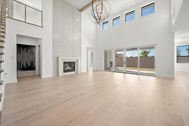 unfurnished living room featuring beamed ceiling, a large fireplace, an inviting chandelier, and light hardwood / wood-style floors