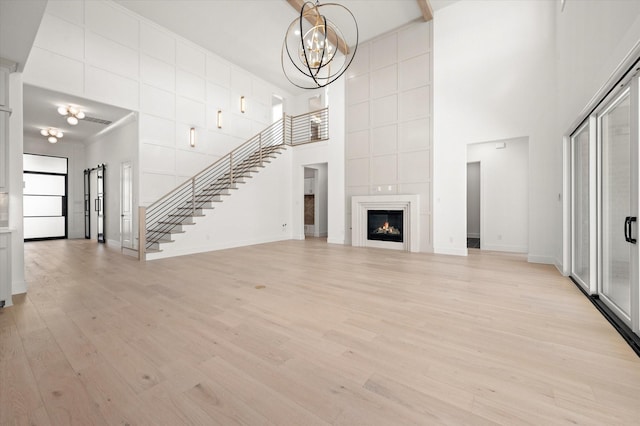 unfurnished living room featuring a tiled fireplace, light hardwood / wood-style flooring, a high ceiling, and an inviting chandelier