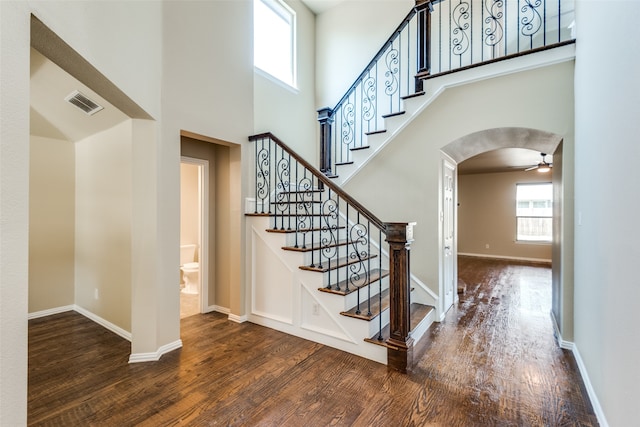 staircase with ceiling fan, hardwood / wood-style floors, and a high ceiling