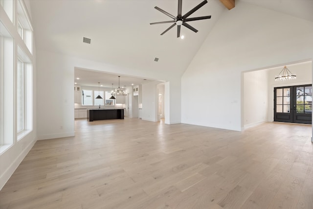 unfurnished living room with high vaulted ceiling, french doors, ceiling fan with notable chandelier, beam ceiling, and light hardwood / wood-style floors