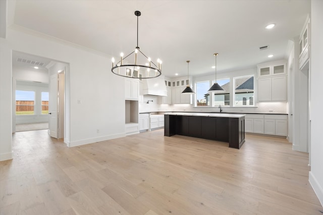 kitchen with ornamental molding, light hardwood / wood-style flooring, white cabinets, a center island, and hanging light fixtures