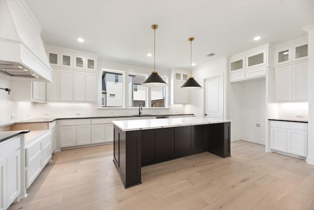 kitchen with white cabinetry, a kitchen island, hanging light fixtures, and light wood-type flooring