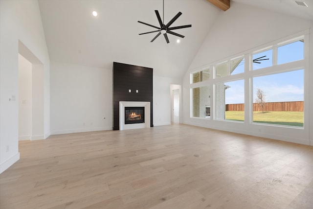 unfurnished living room with high vaulted ceiling, ceiling fan, light wood-type flooring, beamed ceiling, and a large fireplace