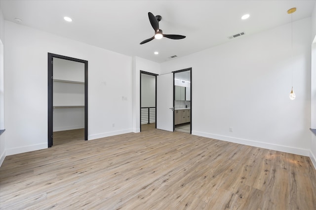 unfurnished bedroom with a walk in closet, ensuite bathroom, ceiling fan, and light wood-type flooring