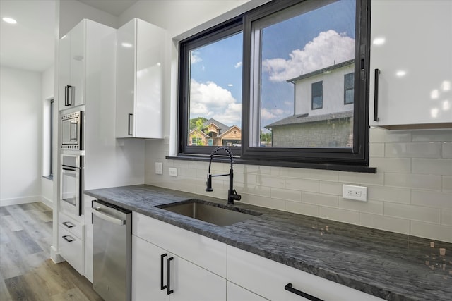 kitchen with sink, appliances with stainless steel finishes, white cabinets, dark stone counters, and light wood-type flooring