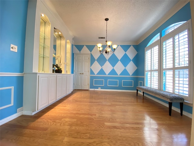 unfurnished dining area with crown molding, light hardwood / wood-style flooring, a textured ceiling, and a notable chandelier