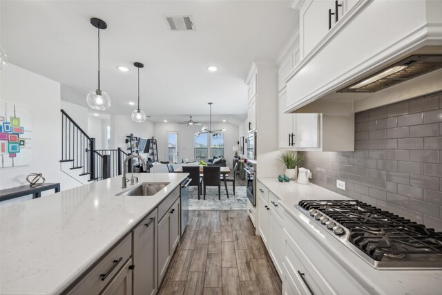 kitchen with sink, dark wood-type flooring, stainless steel appliances, premium range hood, and pendant lighting