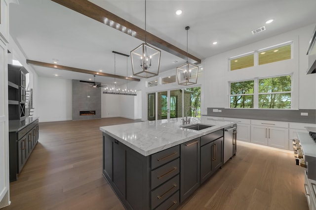 kitchen with light stone countertops, sink, decorative light fixtures, a center island with sink, and a fireplace