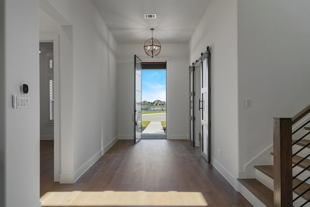 foyer featuring a barn door, dark wood-type flooring, and a notable chandelier