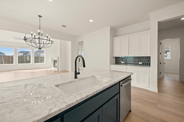 kitchen featuring light stone countertops, sink, hanging light fixtures, stainless steel dishwasher, and light wood-type flooring