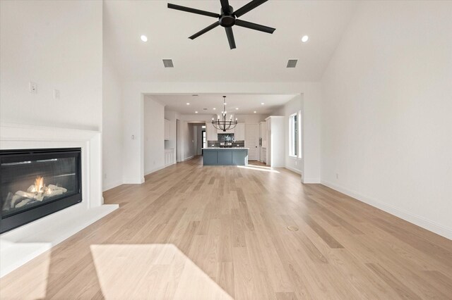 unfurnished living room featuring ceiling fan with notable chandelier, light hardwood / wood-style floors, and lofted ceiling