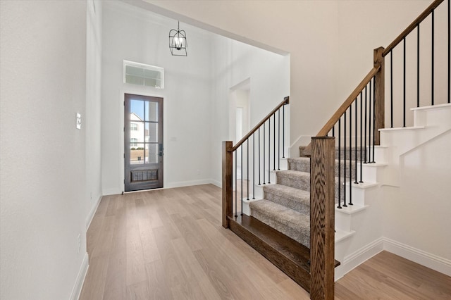 foyer entrance with a towering ceiling, light hardwood / wood-style flooring, and a notable chandelier