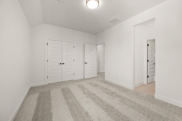 unfurnished bedroom with light carpet, a closet, and lofted ceiling