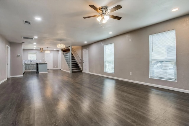 unfurnished living room featuring dark hardwood / wood-style flooring, plenty of natural light, ceiling fan with notable chandelier, and sink