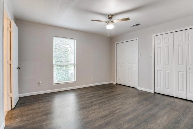 unfurnished bedroom with two closets, dark hardwood / wood-style floors, and ceiling fan