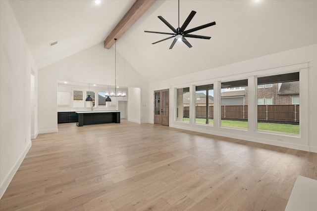 unfurnished living room featuring beamed ceiling, ceiling fan with notable chandelier, light hardwood / wood-style floors, and high vaulted ceiling