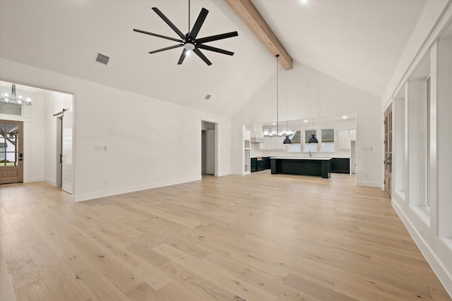 unfurnished living room with a barn door, light hardwood / wood-style flooring, beamed ceiling, high vaulted ceiling, and ceiling fan with notable chandelier