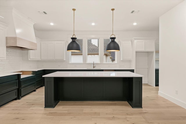 kitchen with white cabinetry, light hardwood / wood-style floors, custom range hood, and decorative light fixtures