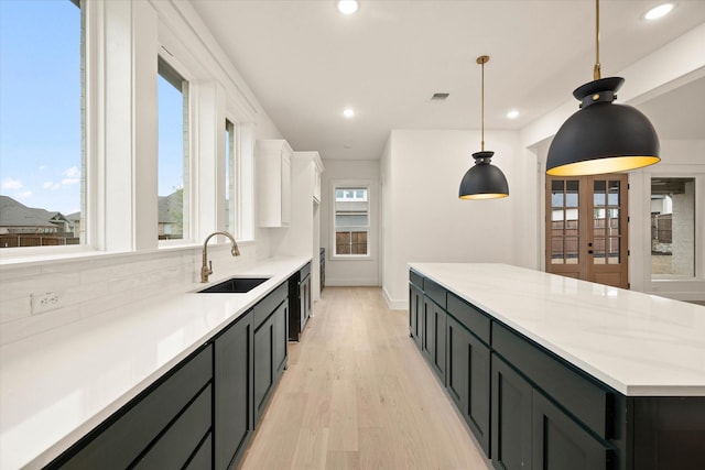 kitchen with light stone countertops, sink, light hardwood / wood-style floors, white cabinetry, and hanging light fixtures