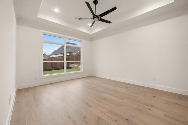 empty room with a raised ceiling, ceiling fan, and light wood-type flooring