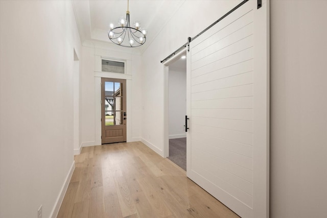 interior space featuring a notable chandelier, a barn door, ornamental molding, and light hardwood / wood-style flooring