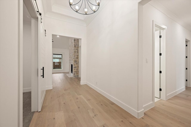 hallway featuring a chandelier, a barn door, light hardwood / wood-style flooring, and crown molding