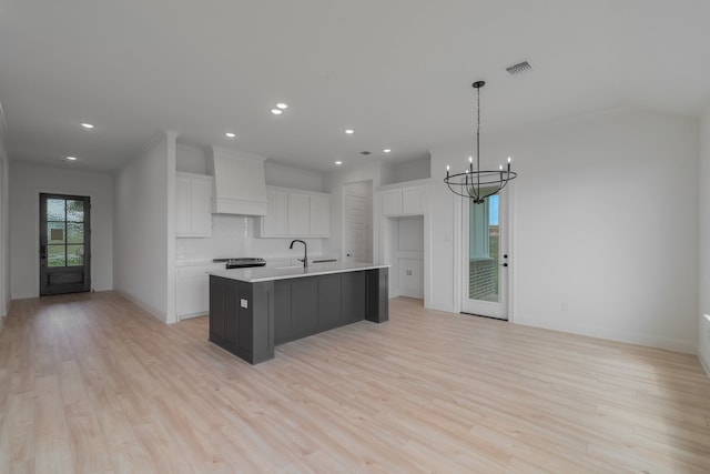 kitchen featuring a kitchen island with sink, wall chimney range hood, hanging light fixtures, and white cabinets