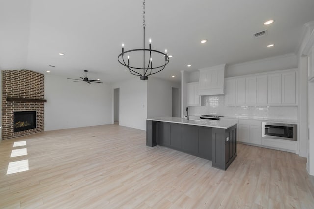 kitchen featuring built in microwave, white cabinetry, a large island with sink, custom exhaust hood, and a brick fireplace