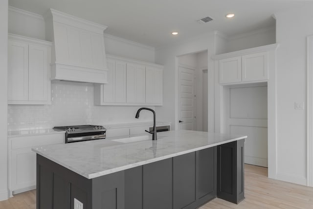 kitchen featuring premium range hood, sink, stainless steel gas stove, white cabinetry, and a large island with sink