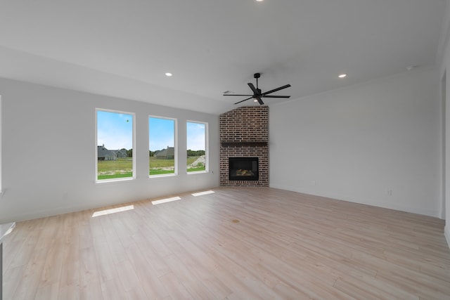 unfurnished living room with ceiling fan, lofted ceiling, a fireplace, and light hardwood / wood-style flooring