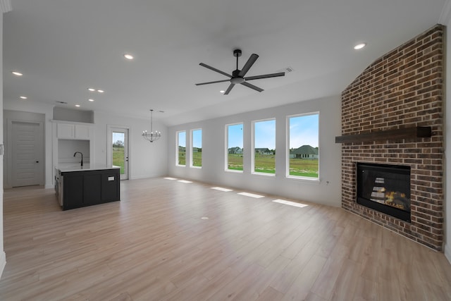 unfurnished living room with sink, light hardwood / wood-style flooring, ceiling fan with notable chandelier, and a brick fireplace