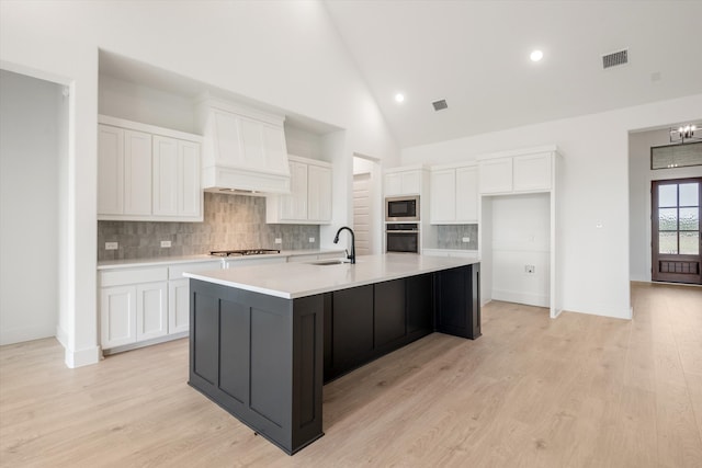 kitchen with built in microwave, white cabinetry, a center island with sink, and wall oven