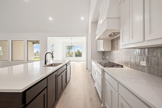 kitchen featuring sink, light stone countertops, custom range hood, white cabinets, and a center island with sink