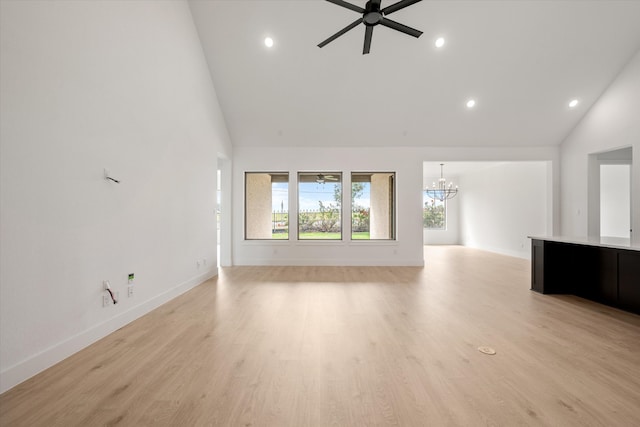 unfurnished living room featuring ceiling fan with notable chandelier, light hardwood / wood-style flooring, and high vaulted ceiling