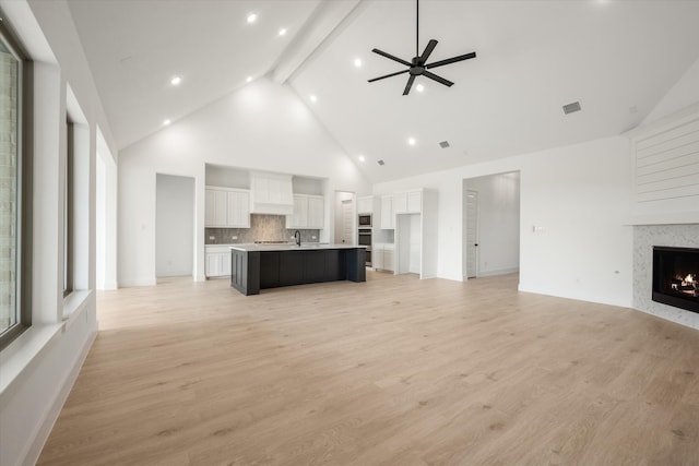 unfurnished living room with high vaulted ceiling, light wood-type flooring, beamed ceiling, ceiling fan, and a fireplace