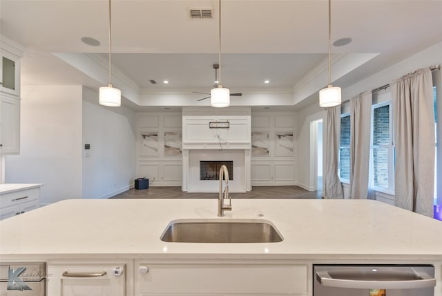 kitchen featuring a raised ceiling, sink, a kitchen island with sink, and decorative light fixtures