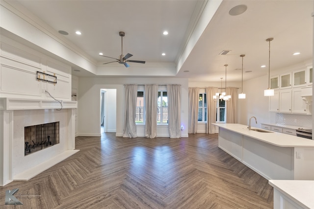 unfurnished living room with sink, dark parquet flooring, a fireplace, ornamental molding, and a raised ceiling