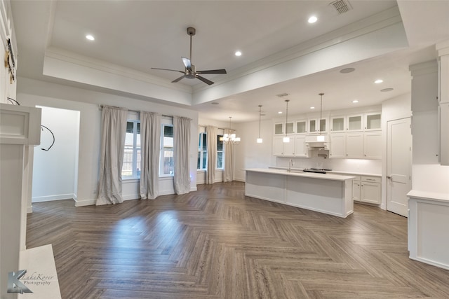 unfurnished living room with crown molding, a tray ceiling, ceiling fan with notable chandelier, and dark parquet floors