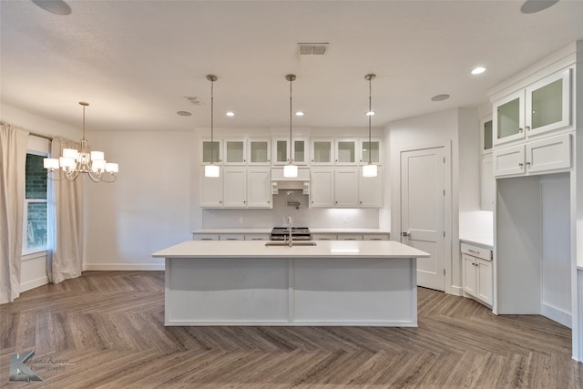 kitchen with decorative light fixtures, decorative backsplash, white cabinets, and a center island with sink