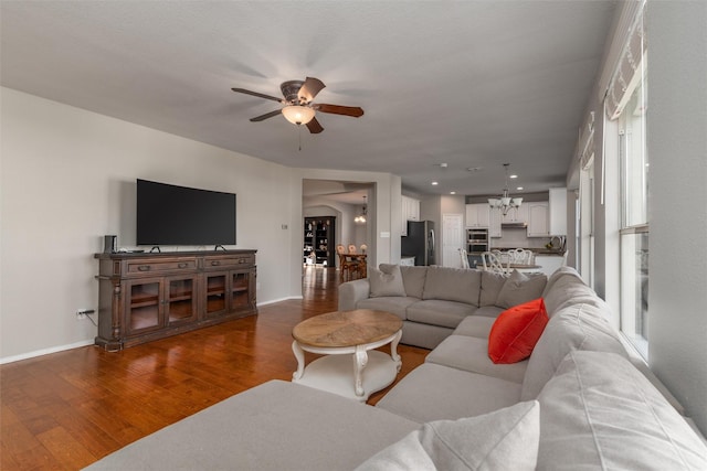 living room with ceiling fan with notable chandelier and dark hardwood / wood-style flooring