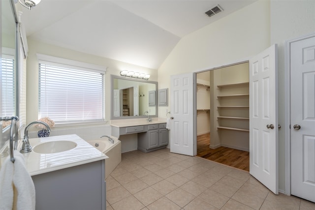 bathroom featuring tile patterned floors, vanity, lofted ceiling, and a tub to relax in