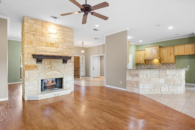 unfurnished living room featuring light hardwood / wood-style flooring, ceiling fan, crown molding, and a stone fireplace