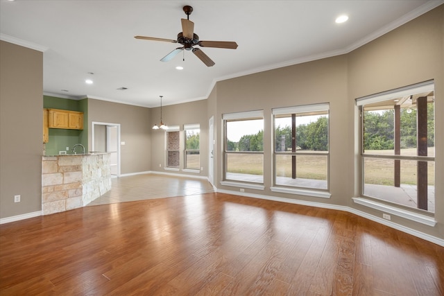 unfurnished living room featuring ornamental molding, a healthy amount of sunlight, ceiling fan with notable chandelier, and light wood-type flooring